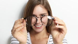 Mulher caucasiana sorri enquanto segura um par de óculos redondos pretos em sua frente