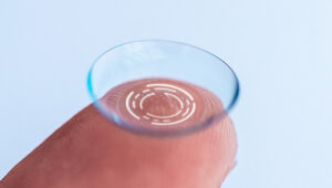 Zoom na ponta de um dedo segurando lente de contato com ilustrações referentes à tecnologia.
