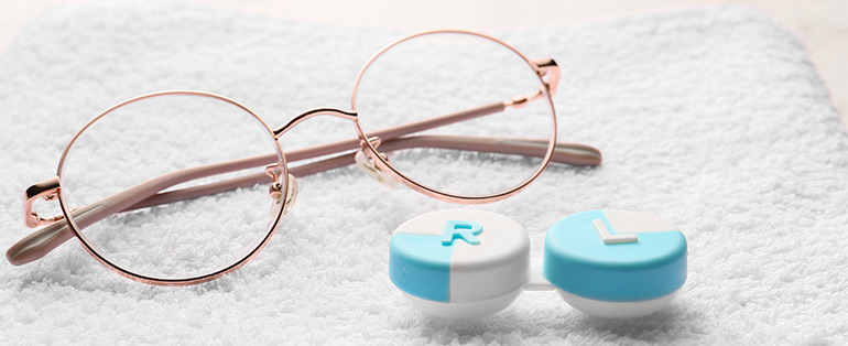 Imagem de óculos de grau redondo com armação na cor dourada. Ao lado direito, um estojo para lentes de contato azul e branco.