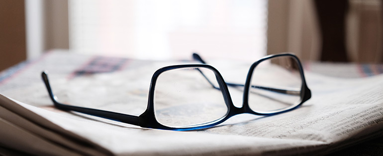 Imagem de óculos de grau quadrado com armação preta apoiado de ponta cabeça em jornal 