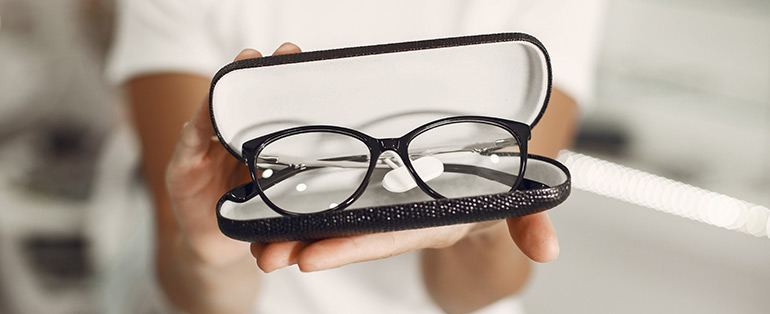 Imagem de mãos caucasianas segurando caixinha de óculos aberta com um modelo dentro. 