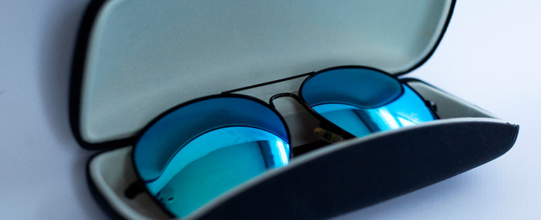 Óculos de sol no formato aviador com lentes espelhadas na cor azul dentro de caixinha protetora. 